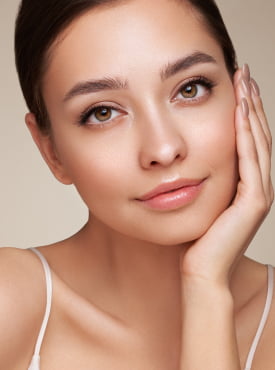 Woman with left hand on her face and looking at the camera. Cropped image focused on her face
